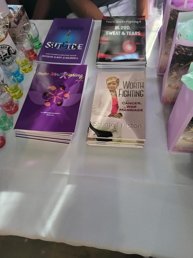 Books displayed on a white tablecloth at an indoor event, including purple and black covers.