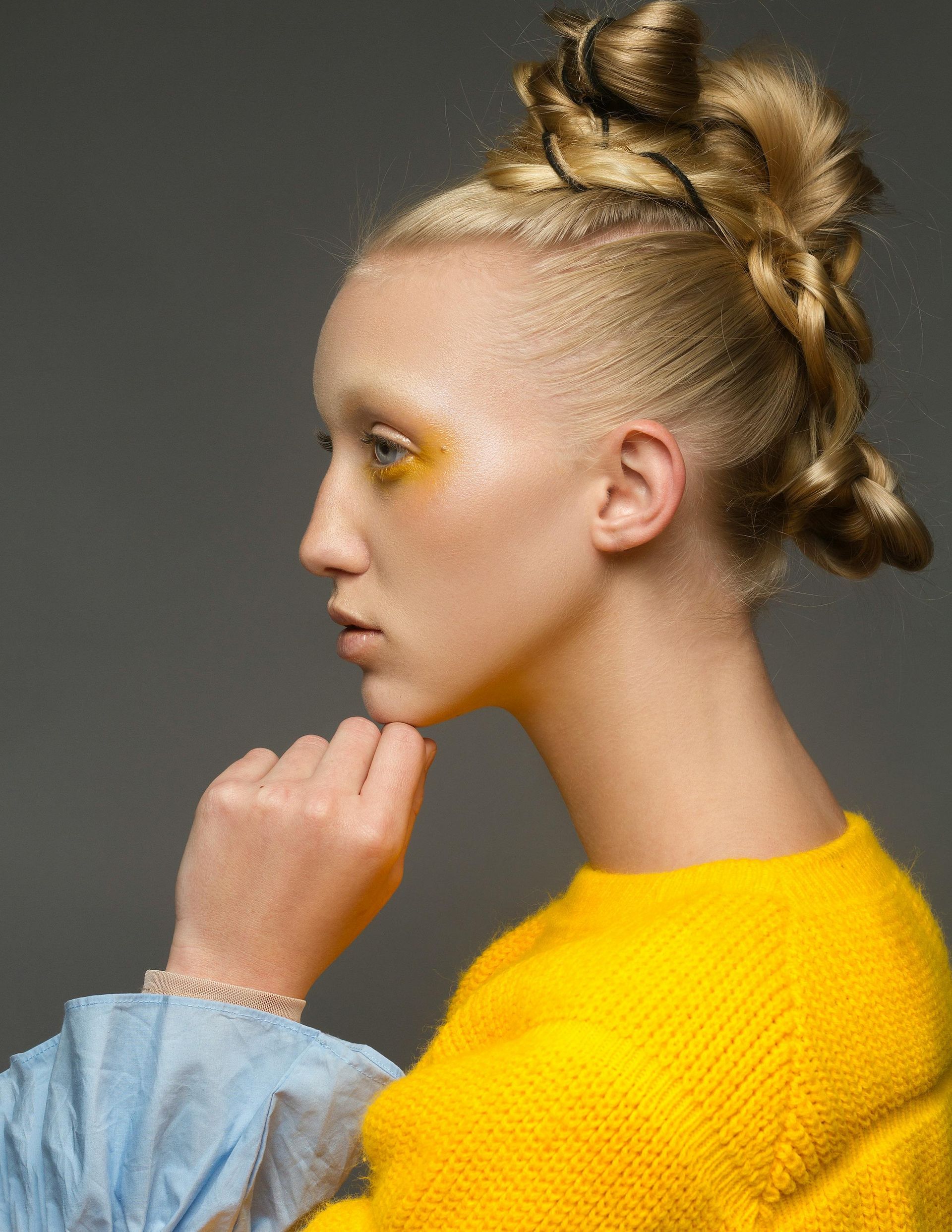 Profile portrait of a person in a bright yellow top with braided updo against a gray background