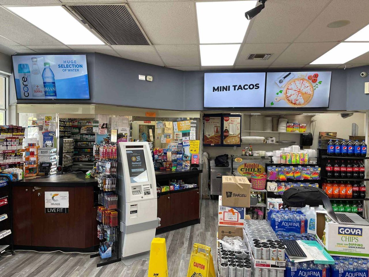 Convenience store checkout with mini tacos sign, beverage coolers, snacks, and a self-service kiosk