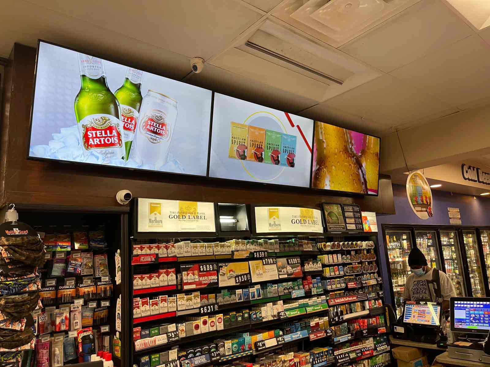 Grocery store aisle with shelves of snacks and drinks beneath bright digital ads above the coolers