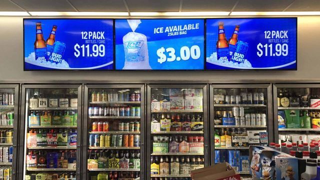 Convenience store drink coolers under blue signs advertising 12-pack $11.99 and ice available $3.00