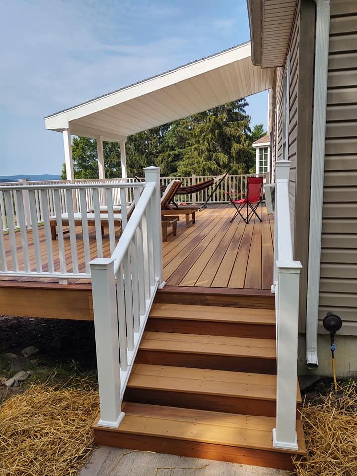 Wooden deck with stairs, white railing, and covered seating area, overlooking trees and water.