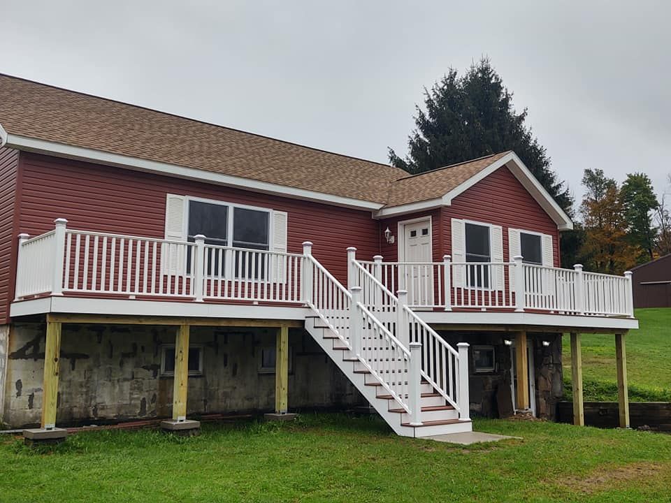 Red house with white deck and stairs on a grassy lawn under an overcast sky.