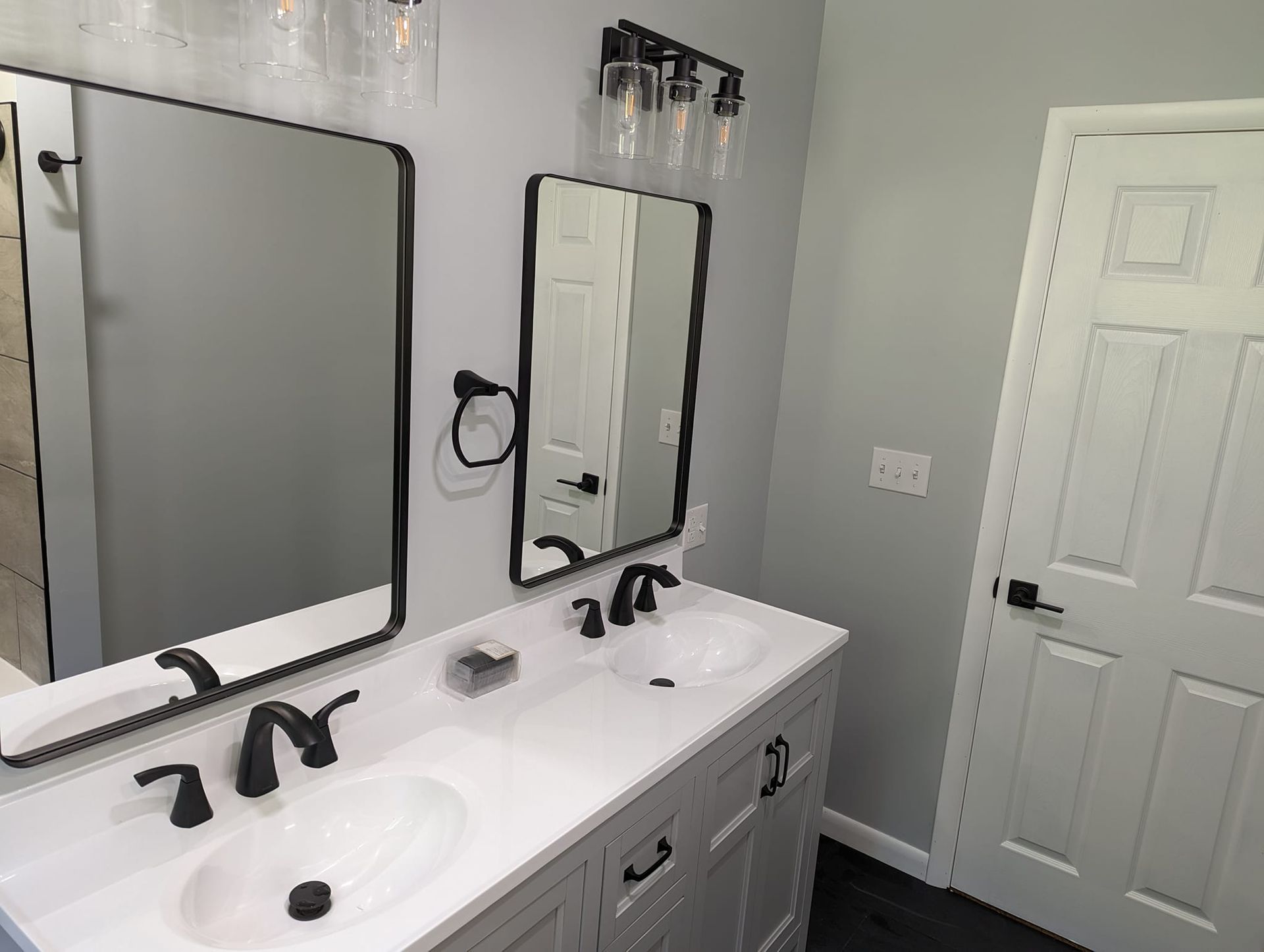 Bathroom with a white vanity, black fixtures, and gray walls; mirrors hang above the sinks.