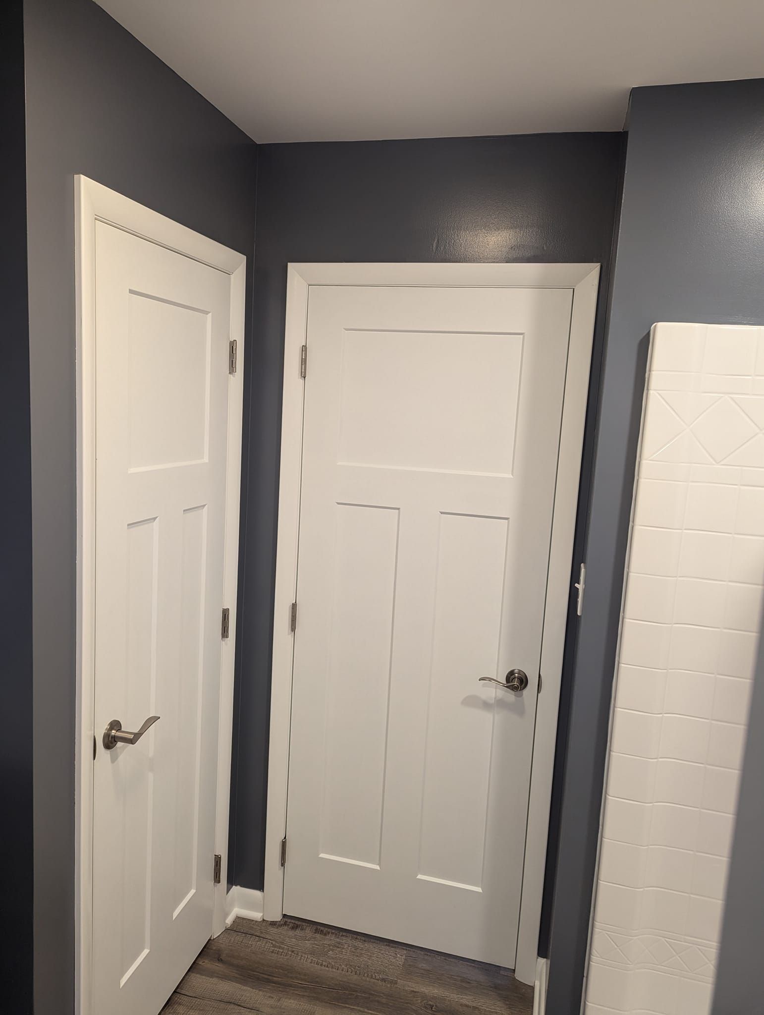 Two white doors in a corner of a room with gray walls and a textured white surface on the right.