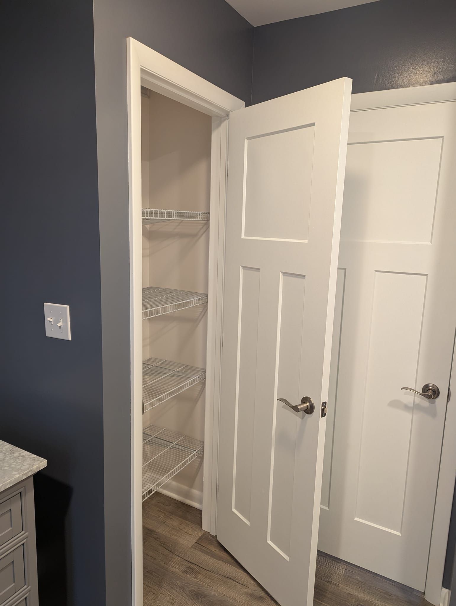 White doors open to reveal wire shelves in a closet, against a blue wall.