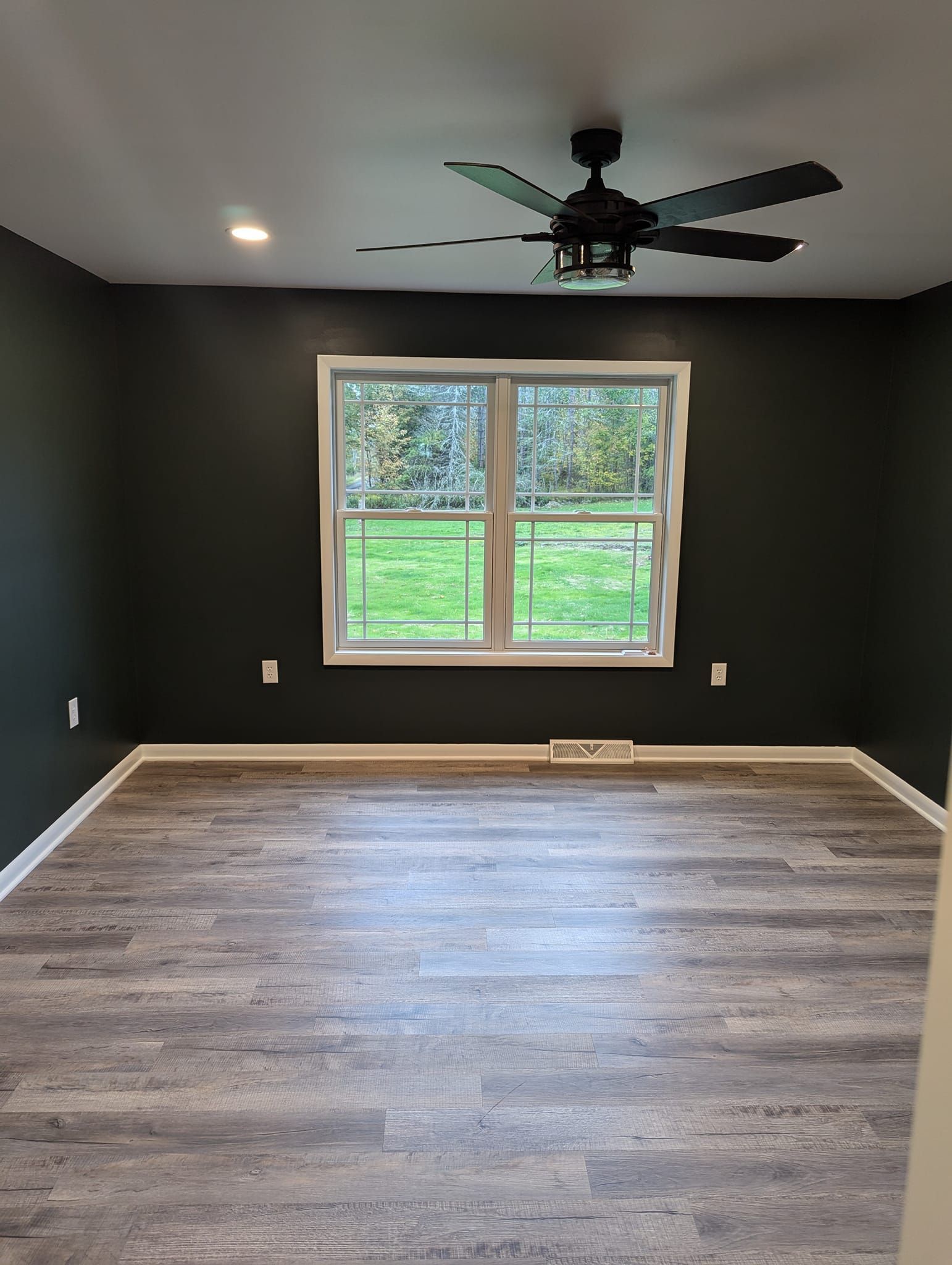 Empty room with dark gray walls, a window, wood-look floor, and a ceiling fan.