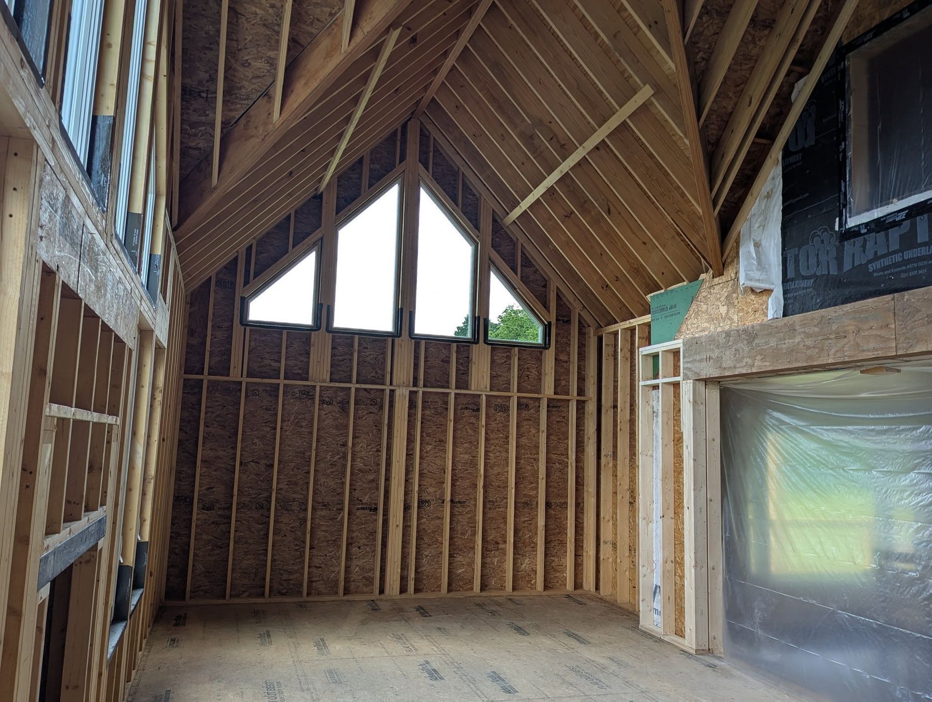 Interior of a house under construction; wooden frame walls, angled ceiling with triangular window.