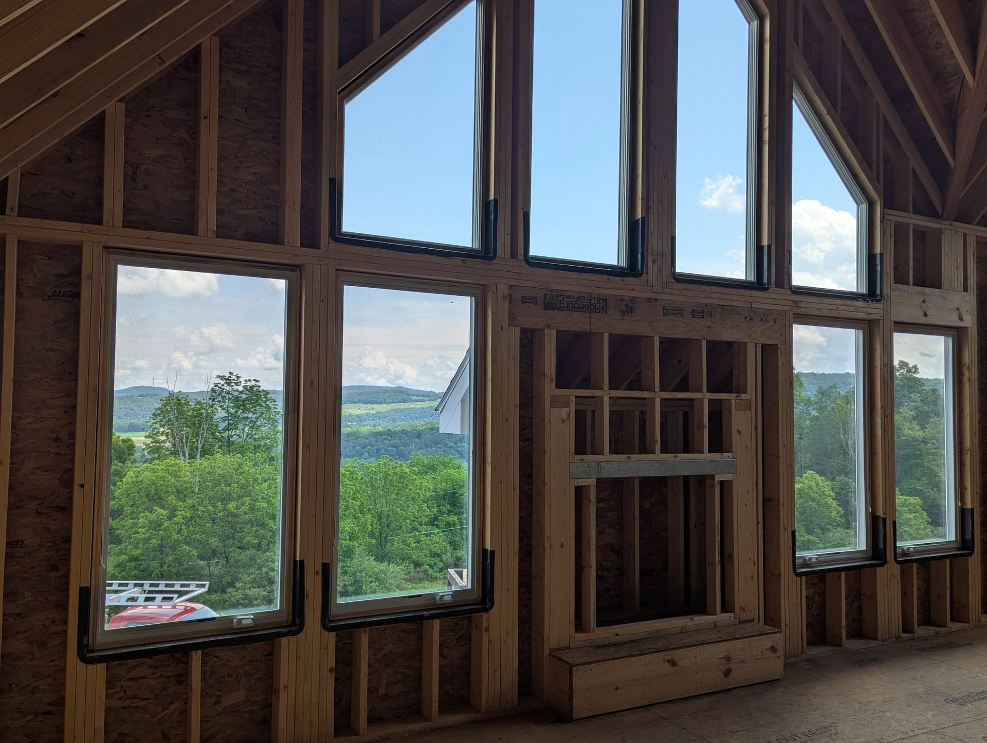 Interior of a house under construction with a large window and fireplace framing a scenic outdoor view.