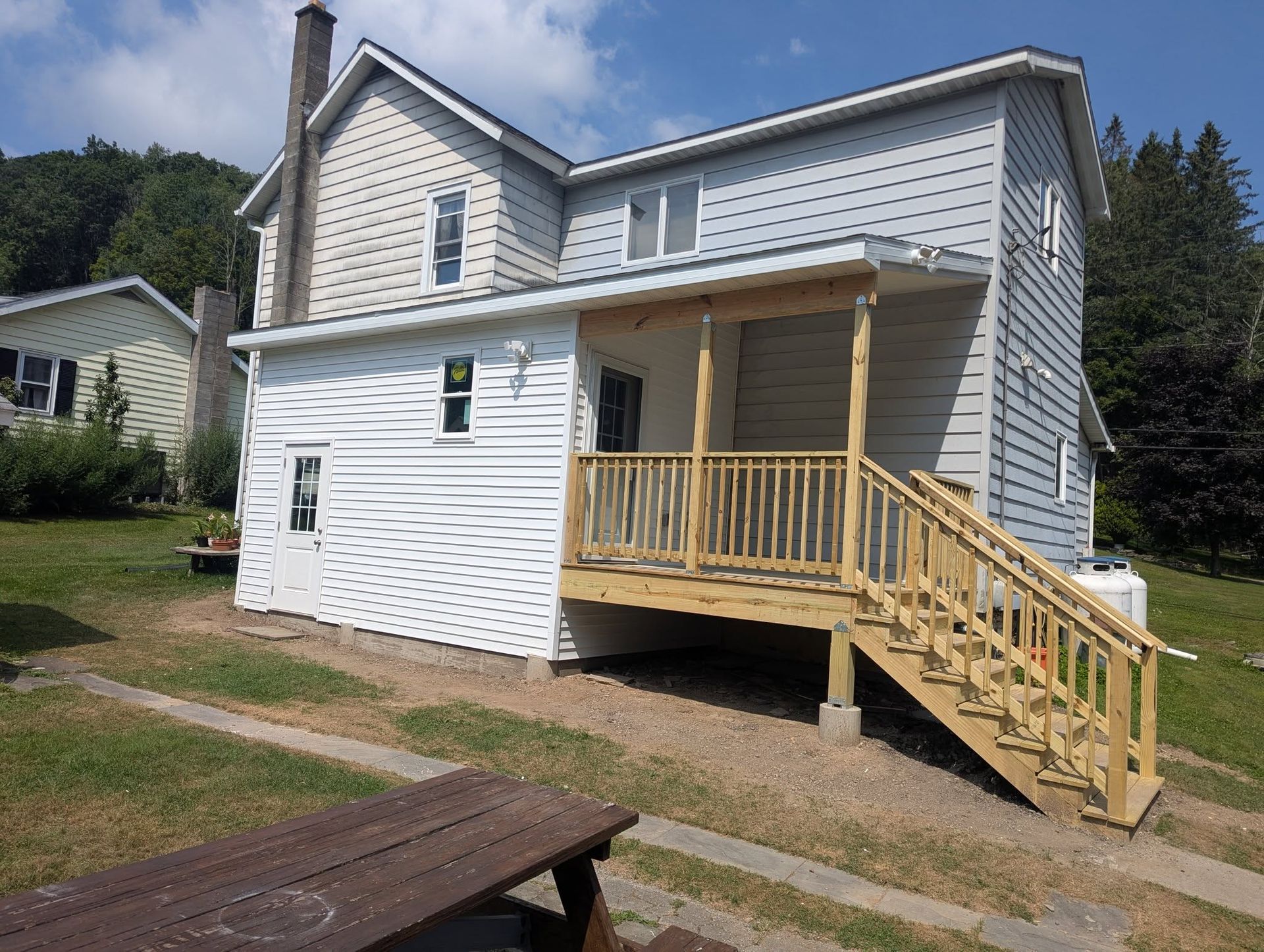 Two-story house with a wooden porch and steps, light blue siding, and a picnic table in the yard.