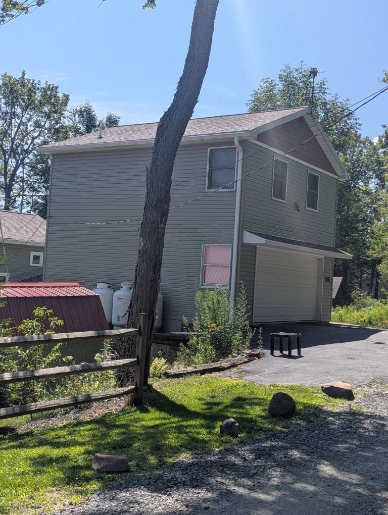 Two-story green house with attached garage, propane tanks, and a tree in front.
