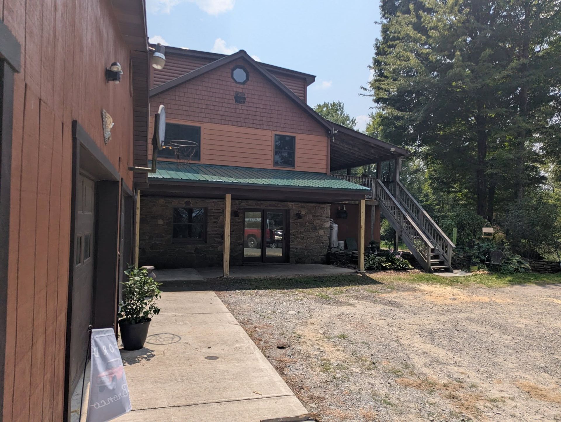 Two-story building with brown siding and green roof, porch, and a staircase. Gravel parking area.