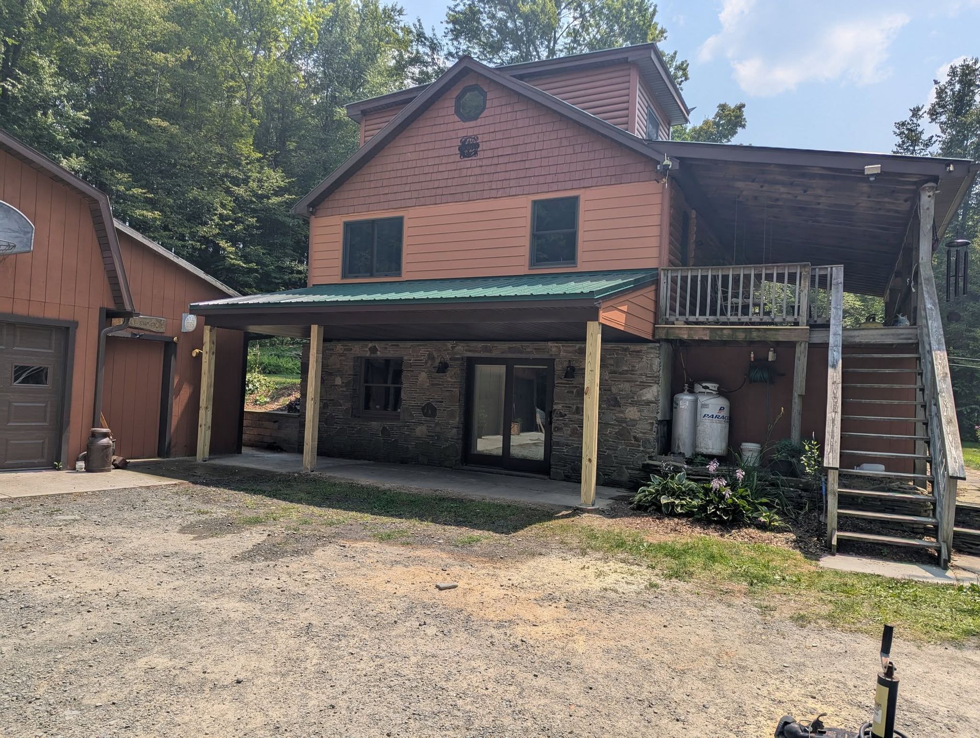 Rustic two-story building with stone and brick, covered porch, deck with stairs, and a gravel driveway.