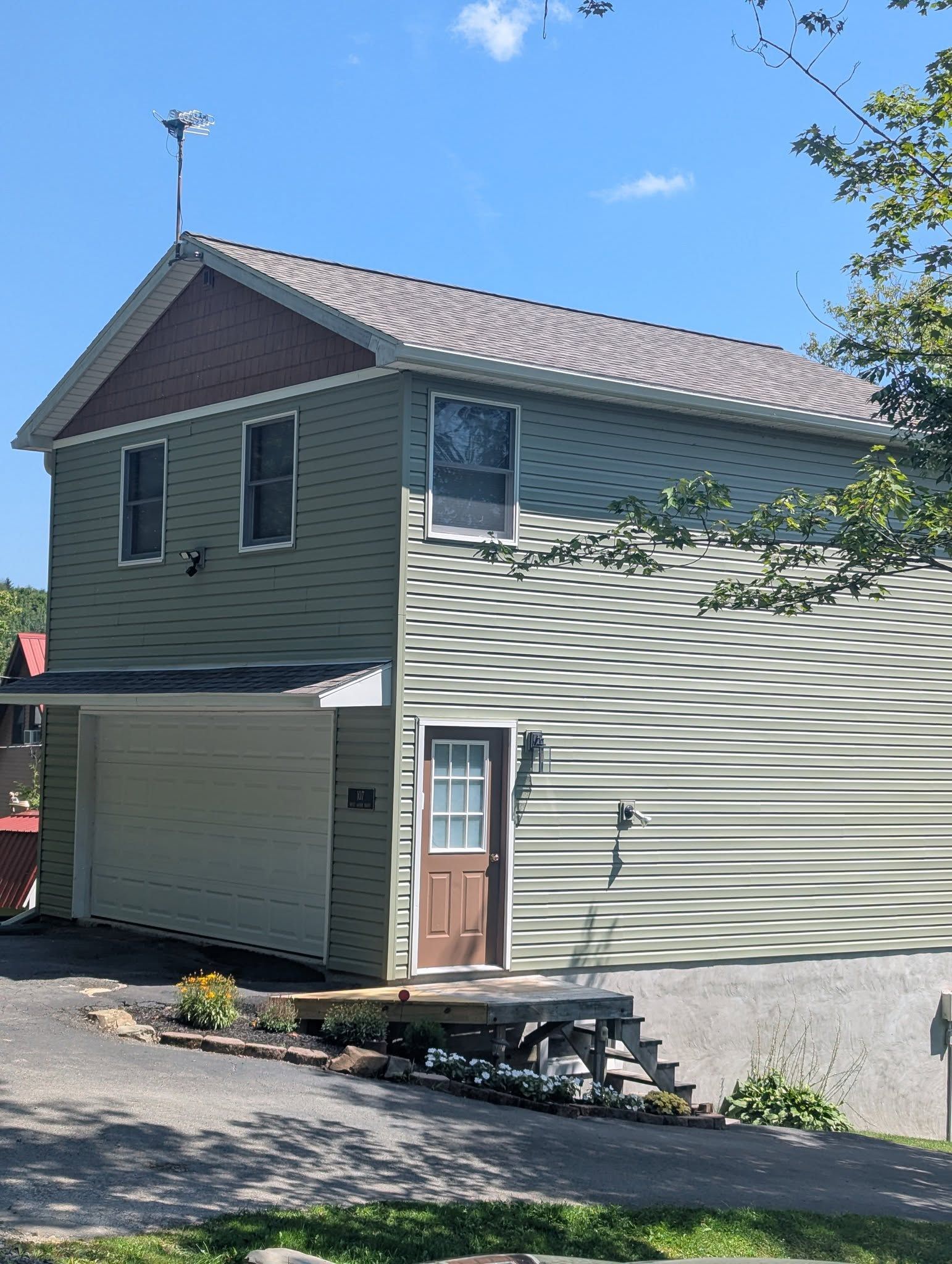 Two-story house with green siding, brown door, garage, and antenna. Sunny day.