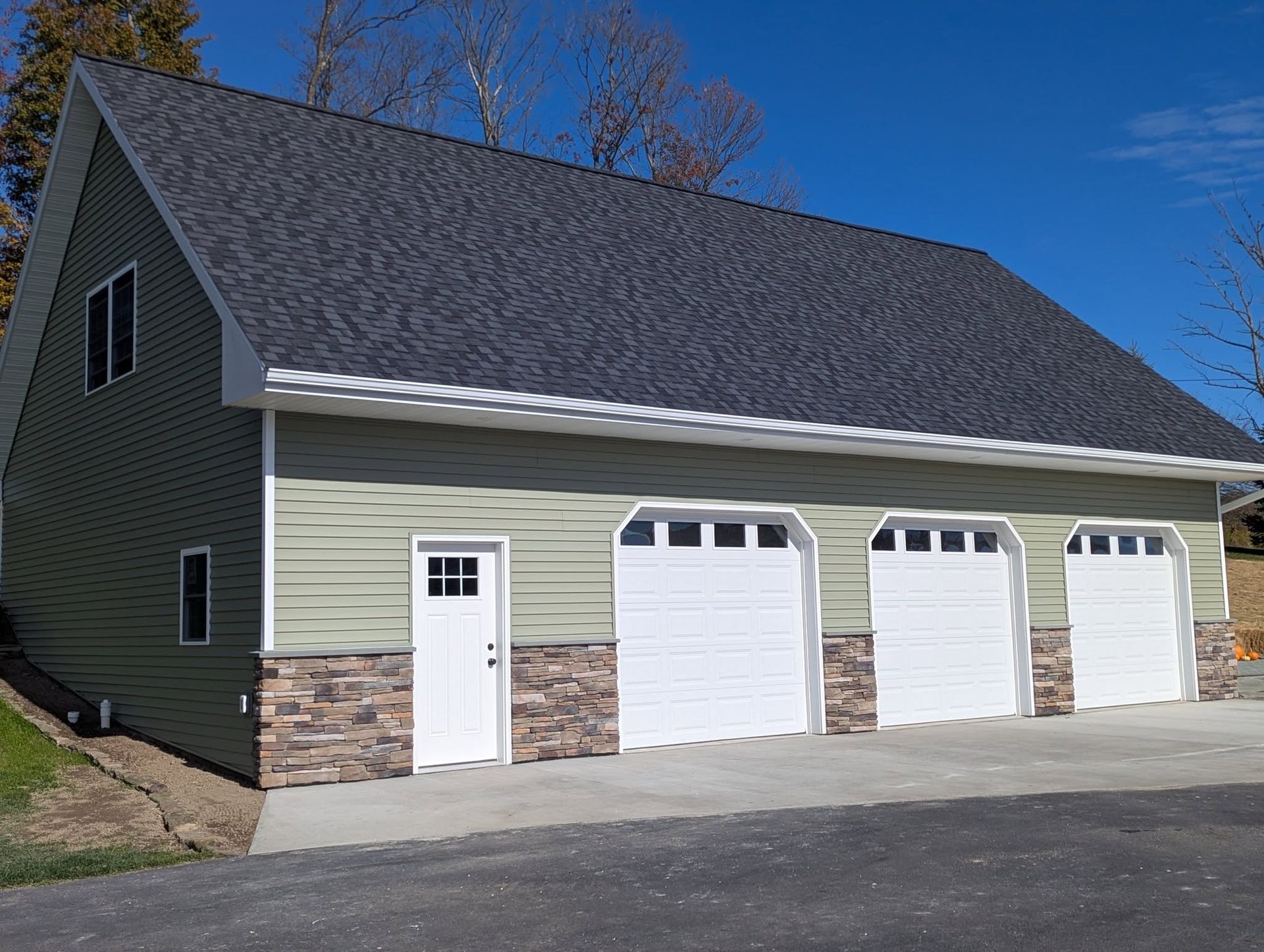 Green and stone-trimmed garage with three white garage doors and a white entry door under a dark gray roof.
