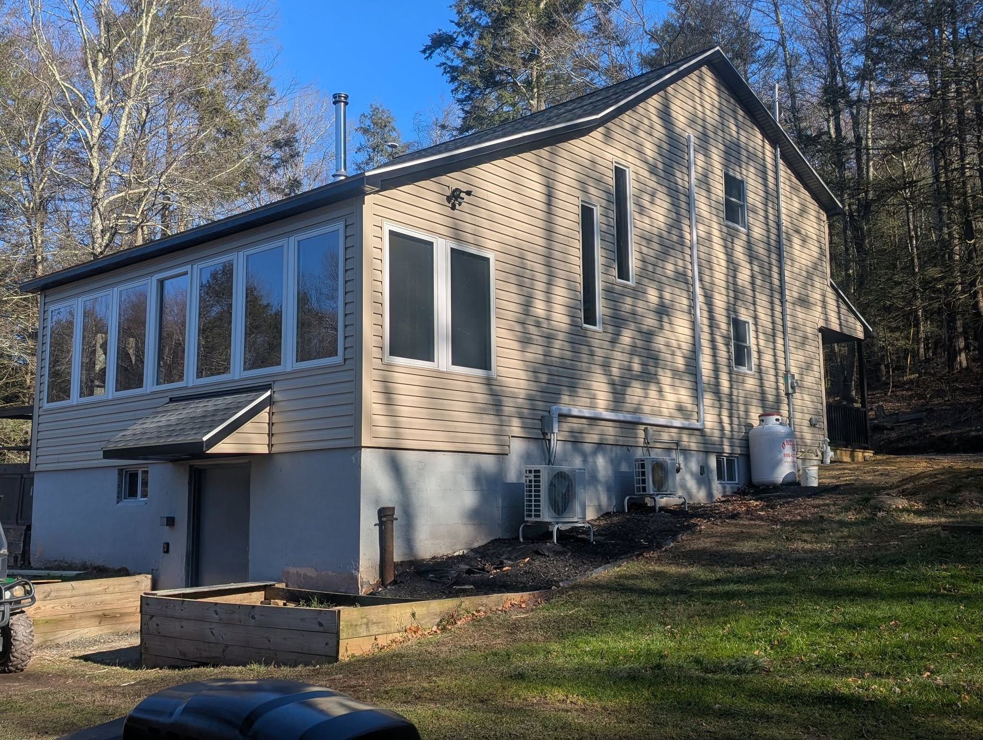 Beige two-story house with screened-in porch, surrounded by trees, and partial concrete foundation.