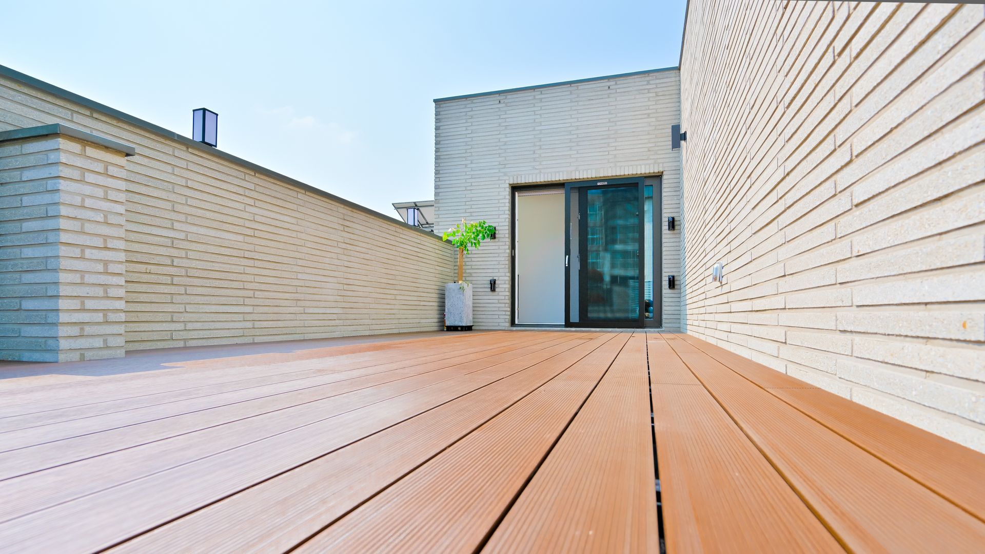 Wooden deck leads to a building entrance with glass doors, under a blue sky.