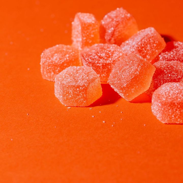 A person is holding a piece of orange candy in their hand.