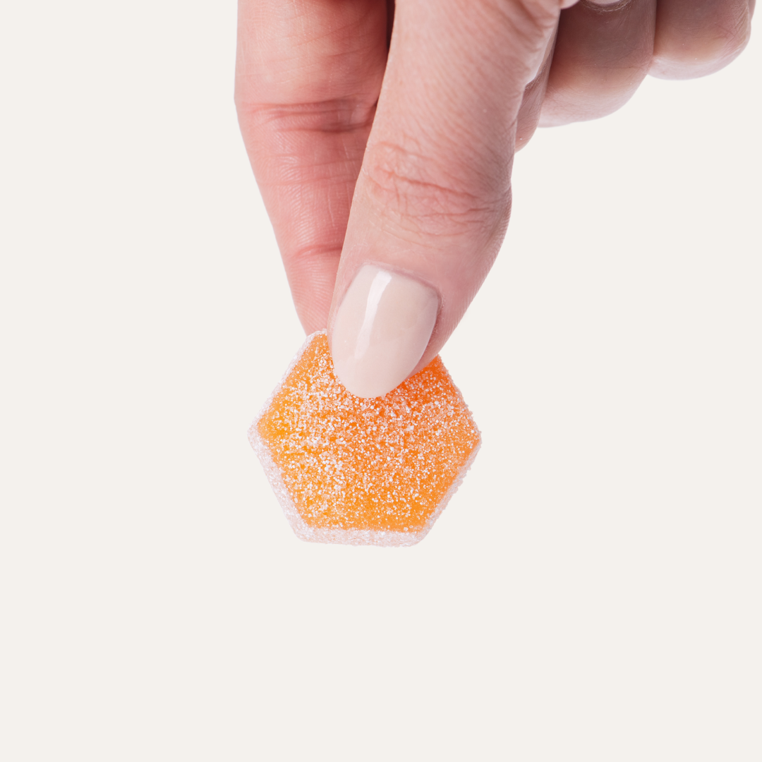 A person is holding a piece of orange candy in their hand.