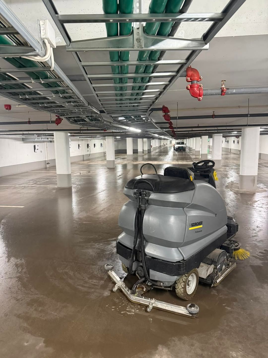 Riding floor scrubber on a wet underground parking garage floor under exposed pipes and sprinklers