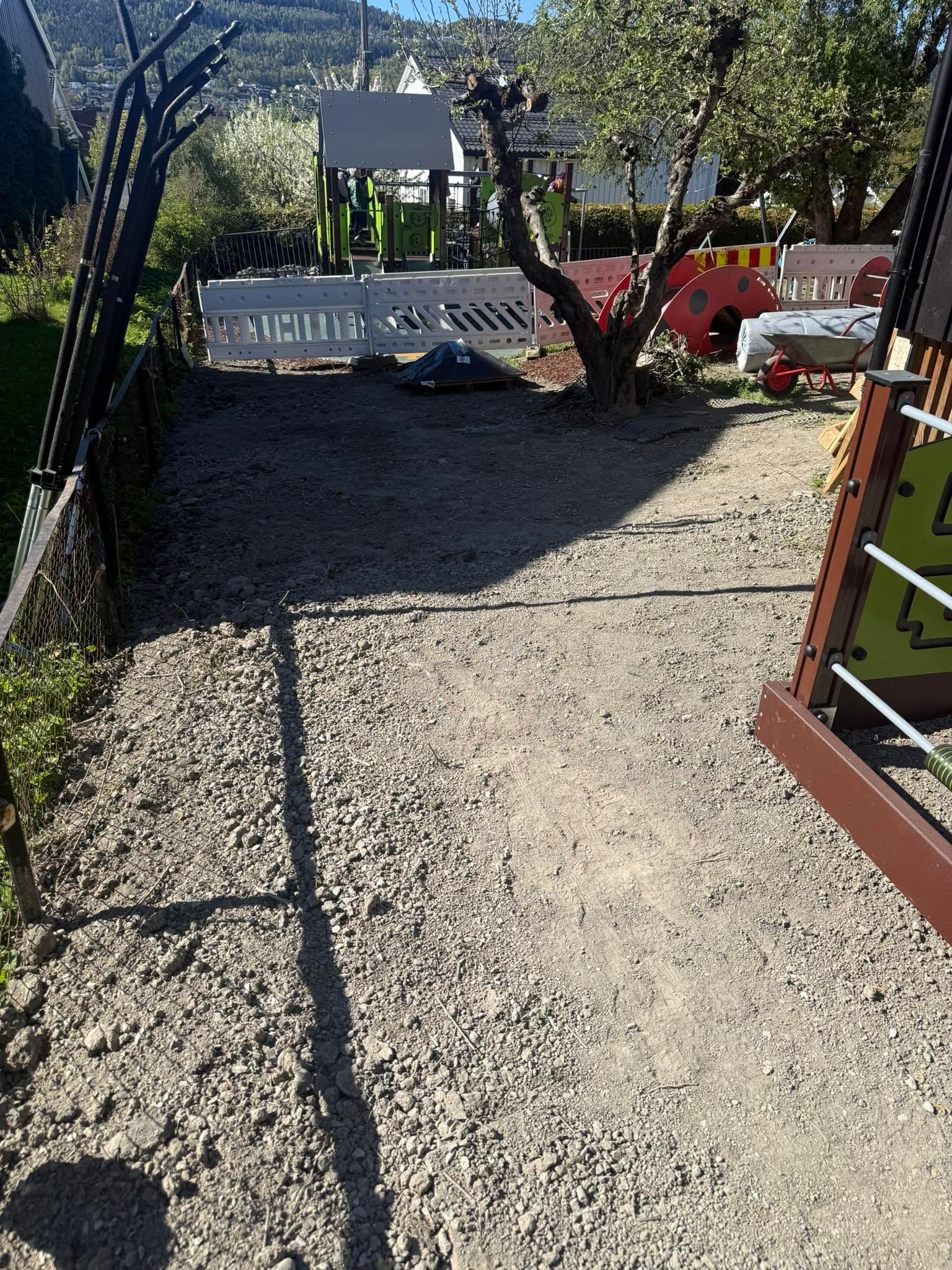 Gravel path leading to a sign and playground equipment in a sunny outdoor park