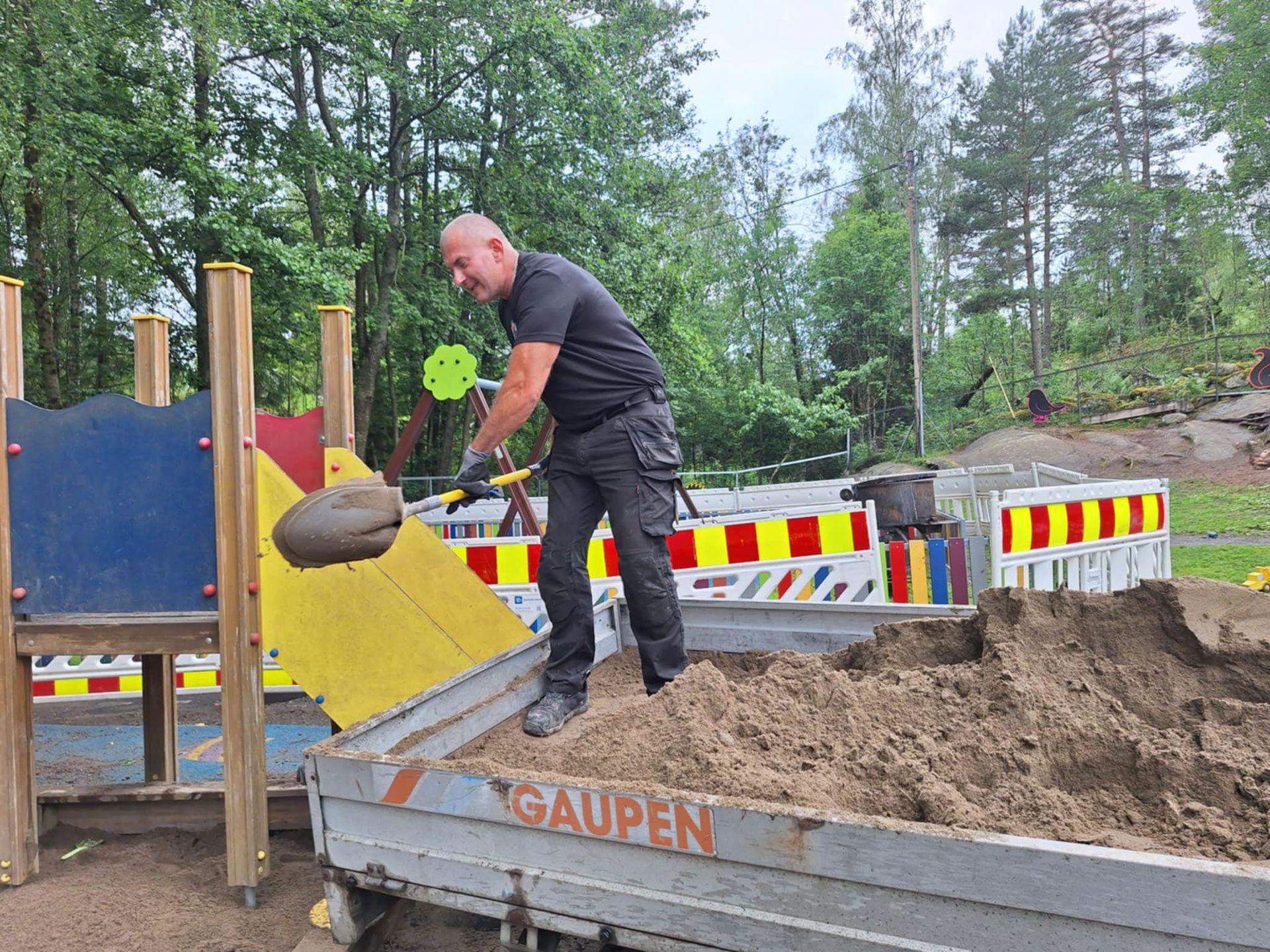 Mann som måker sand fra en lastebil og ut på en lekeplass. Lastebilen har ordet «GAUPEN» på seg.