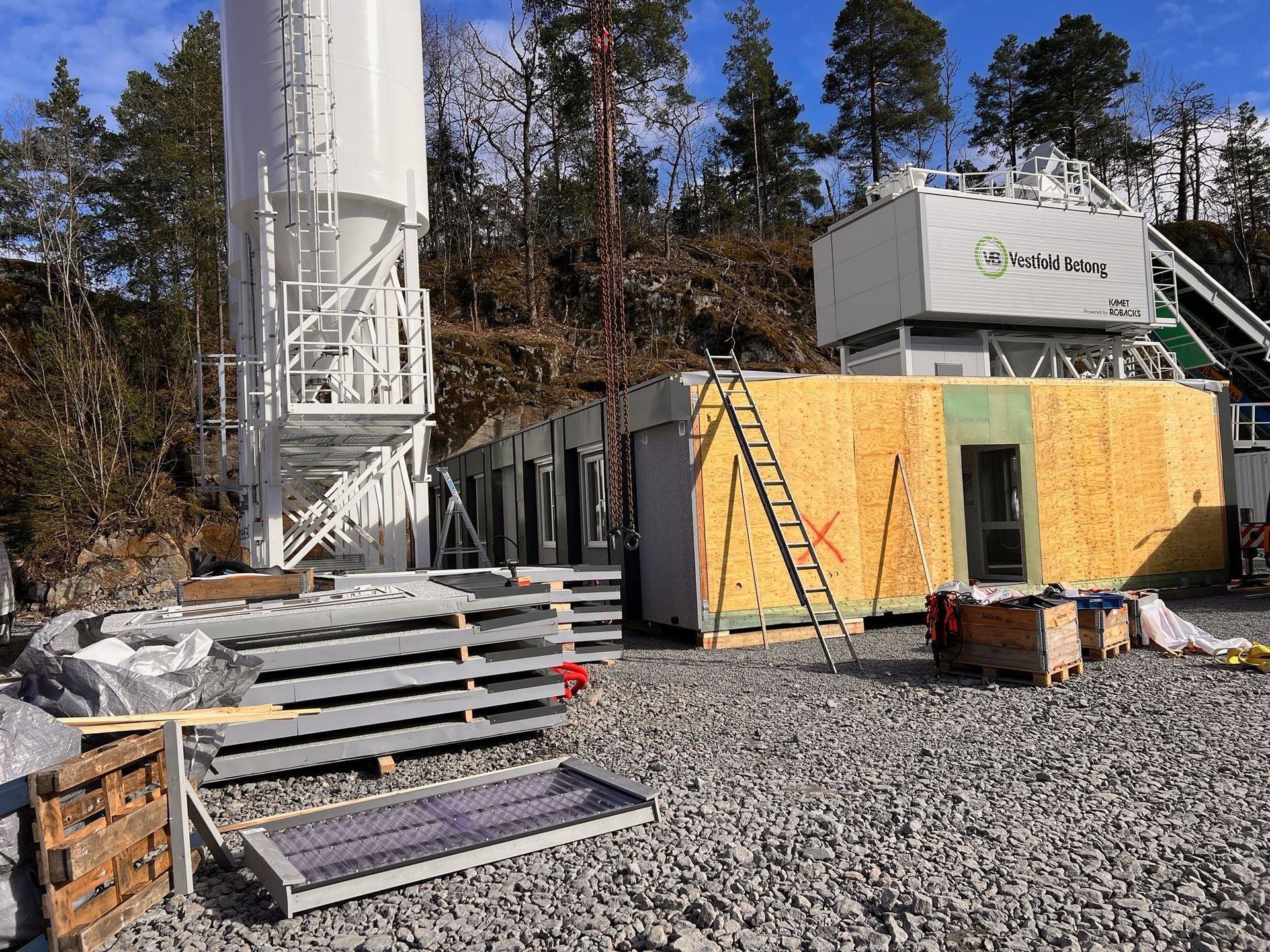 Construction site with modular building, crane, stairs, and gravel lot in wooded area
