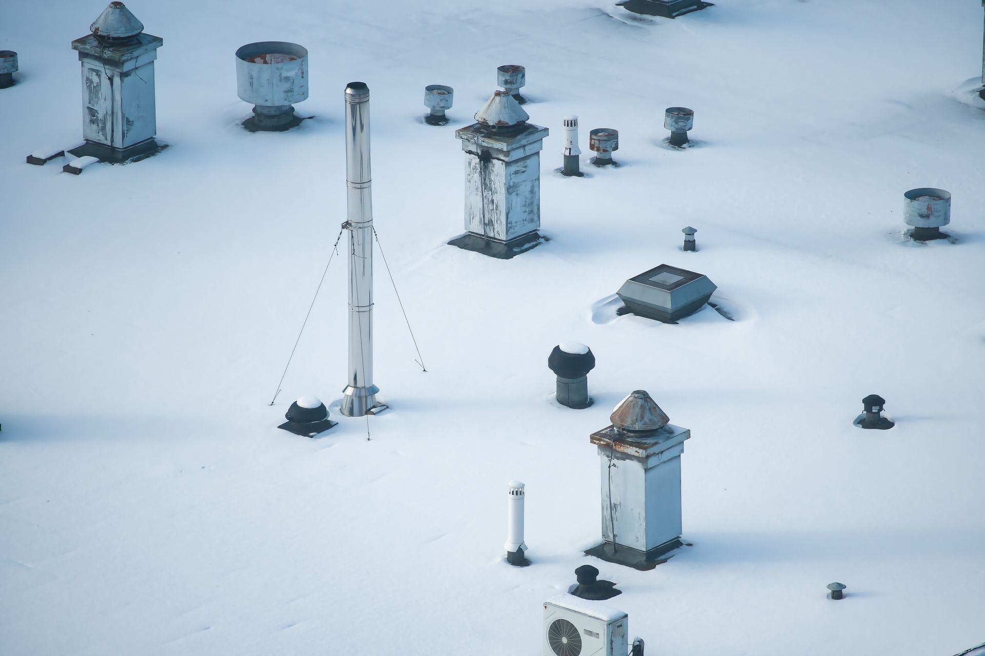 Toit enneigé avec de multiples conduits de ventilation et cheminées sous un ciel pâle