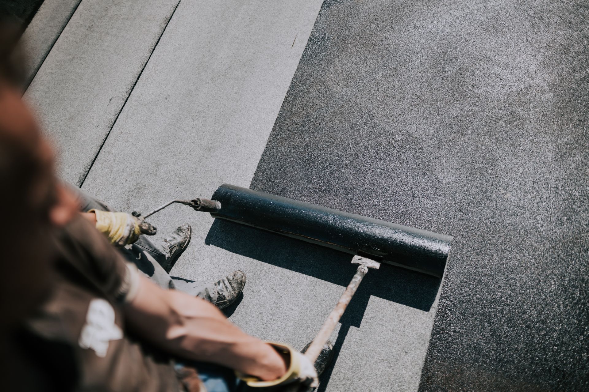 Une personne utilise un rouleau à peinture pour recouvrir un sol gris dans un environnement intérieur