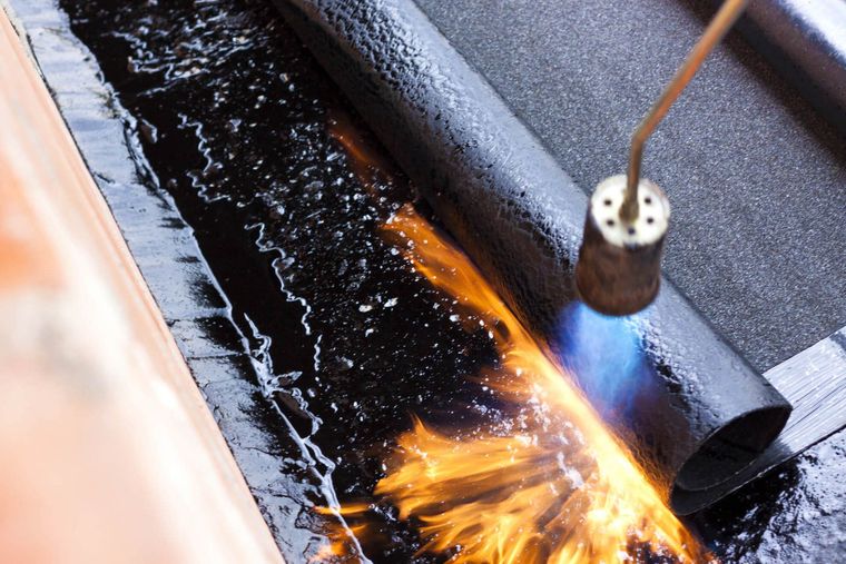 Une torche applique la flamme sur le joint de toiture, faisant fondre le matériau d'étanchéité noir et projetant des étincelles.