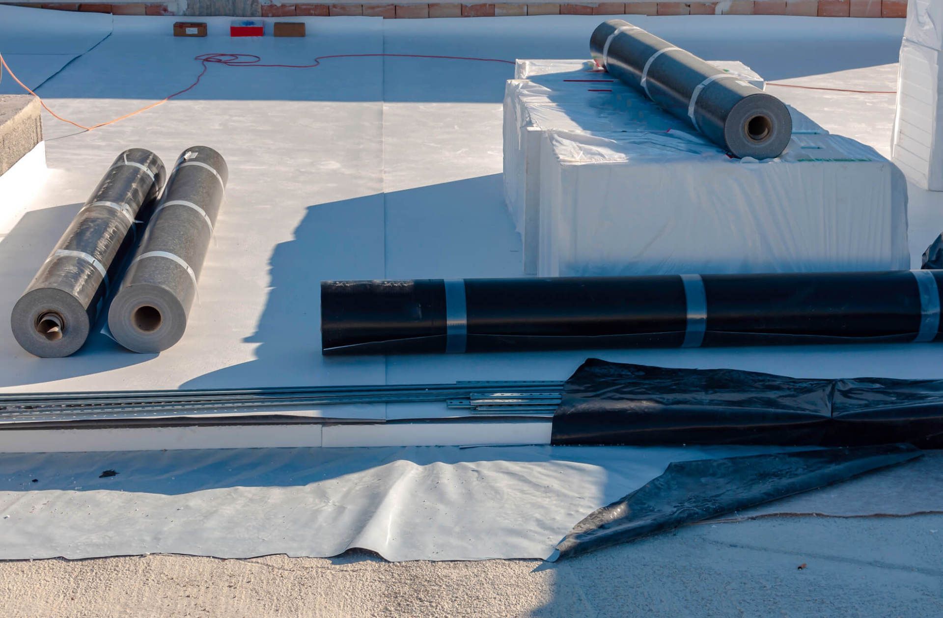 Roofing materials and rolls of underlayment laid out on a flat rooftop in sunlight