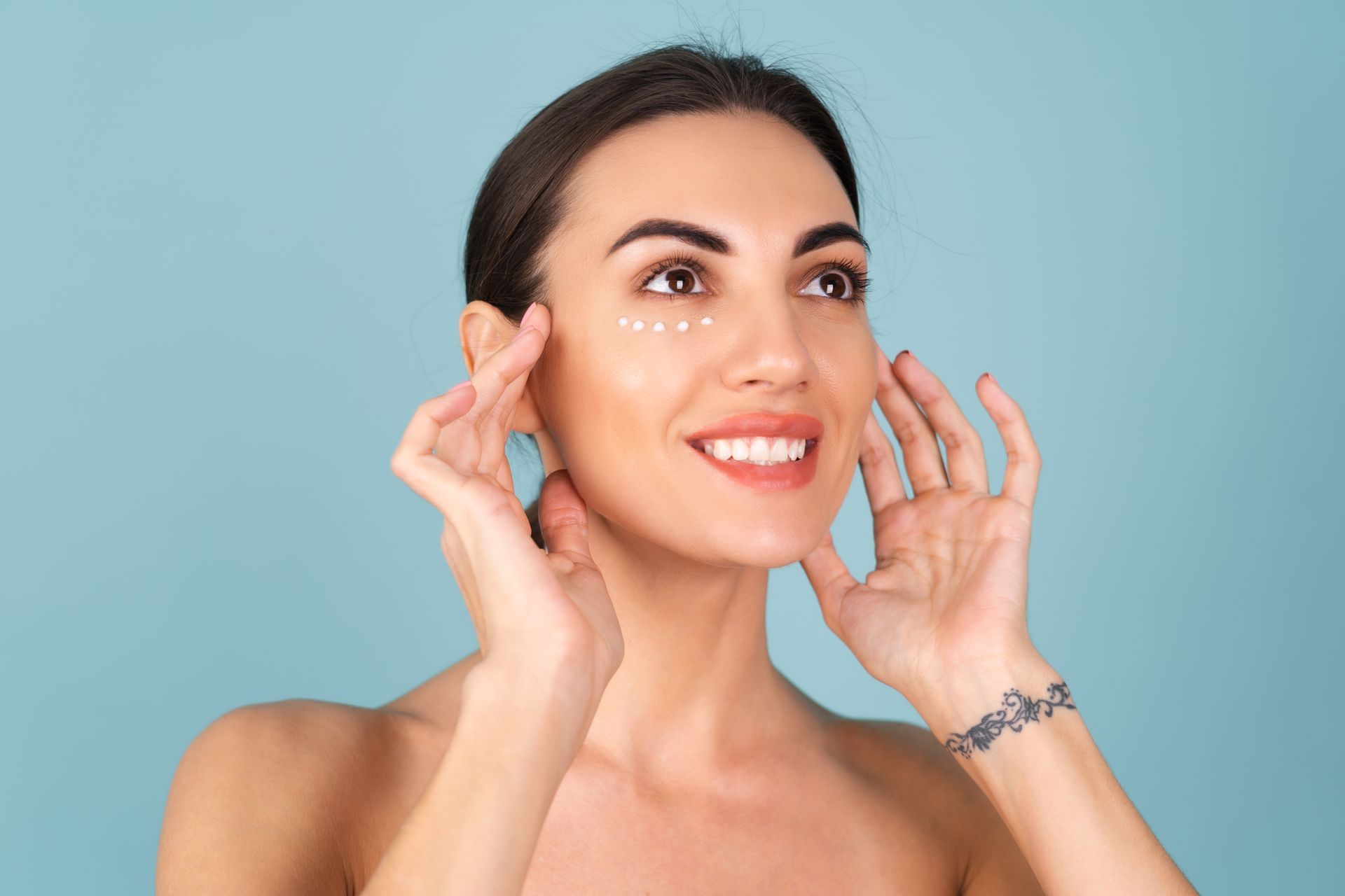 Smiling woman in a strapless top touching her face against a light blue background