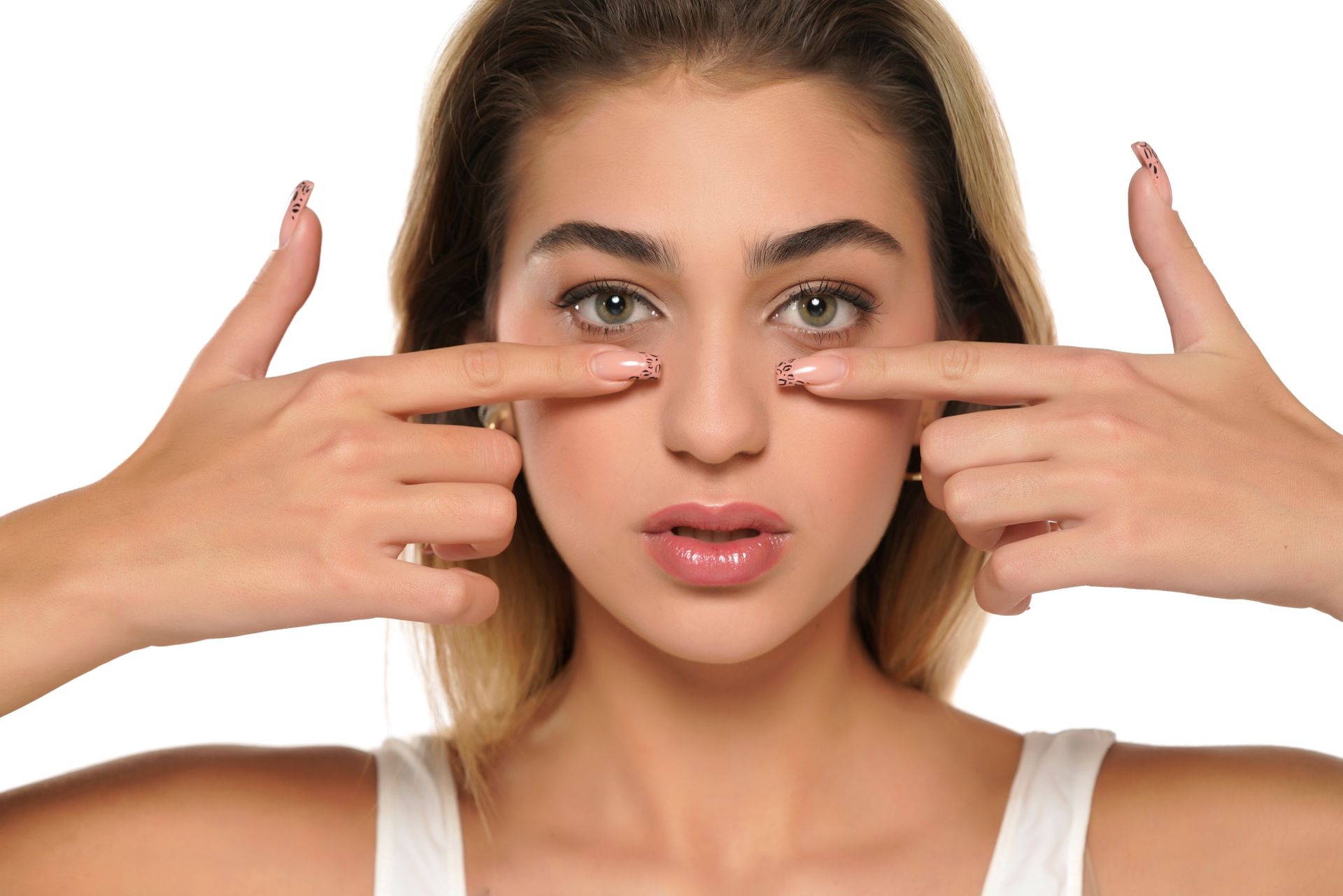 Woman pointing fingers under her eyes, looking at the camera. She has long nails and light hair.