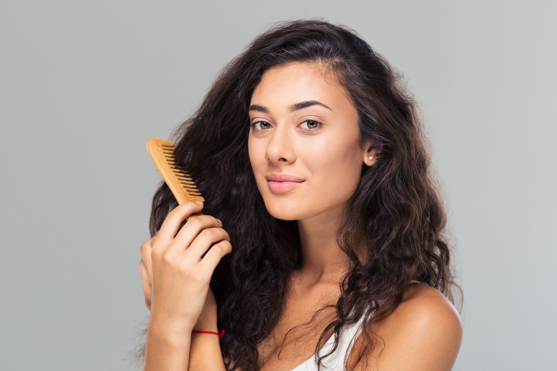 Woman with curly hair holding a comb against a gray background
