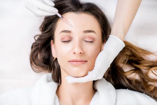 A woman is getting a botox injection in her forehead.