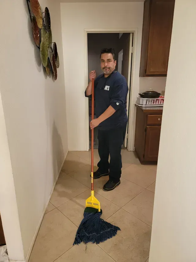 Person mopping a tiled hallway with a blue mop and yellow wringer bucket.