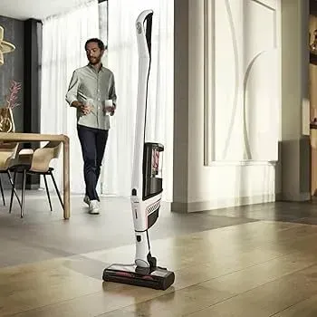 Cordless upright vacuum in a bright modern room with a person walking in the background Cordless upright vacuum in a bright modern room with a person walking in the background