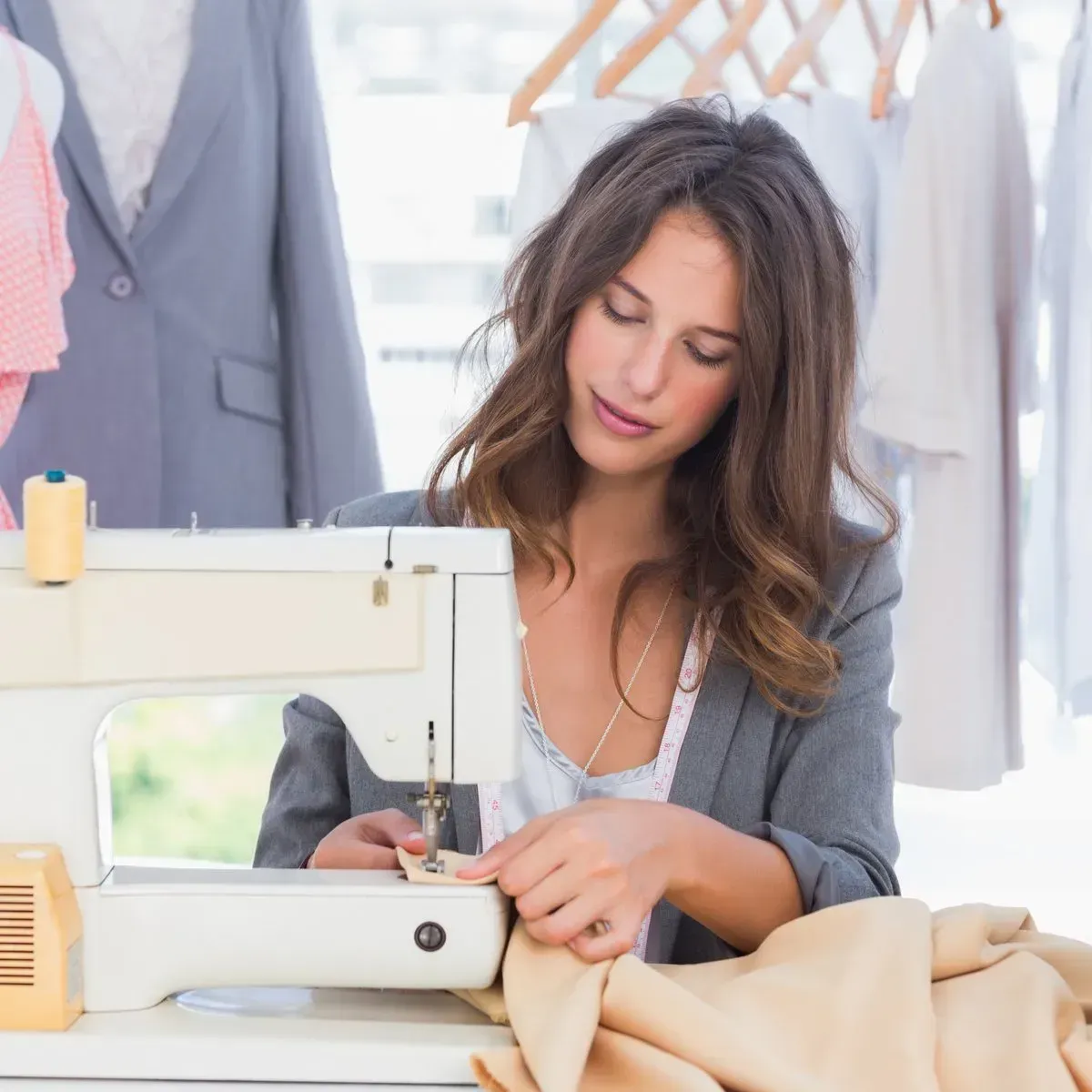 Woman sewing beige fabric on a sewing machine in a bright clothing workshop