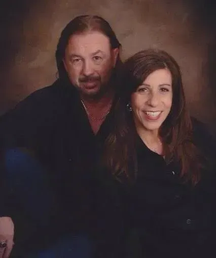 Studio portrait of a smiling couple in dark clothing against a warm brown background