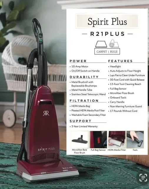 Maroon upright vacuum beside product info card on green carpet, with basket and lamp in the background Maroon upright vacuum beside product info card on green carpet, with basket and lamp in the background