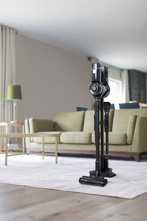 Maroon upright vacuum cleaner beside product box labeled Spirit Plus R21PLUS on a green rug.