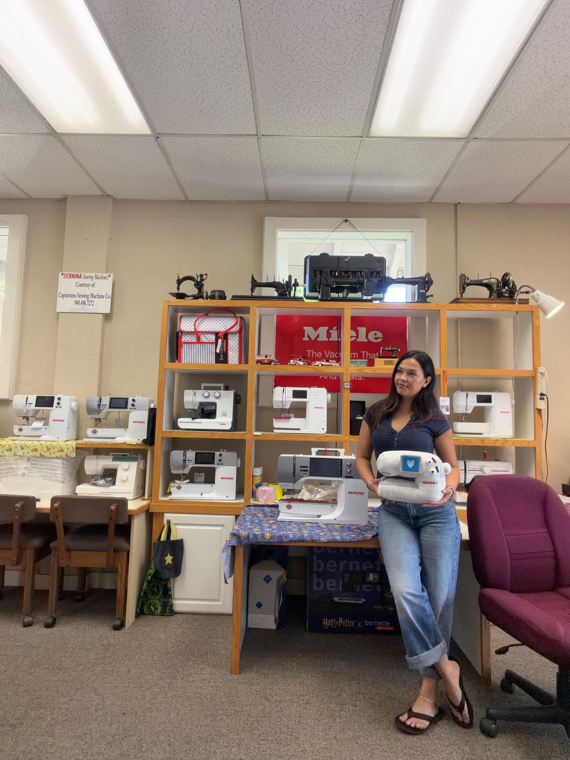 Woman seated in a storage room holding a box, with shelves of supplies and office furniture behind her