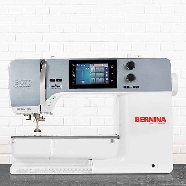 White Bernina sewing machine on a white brick background, front view with built-in display and controls
