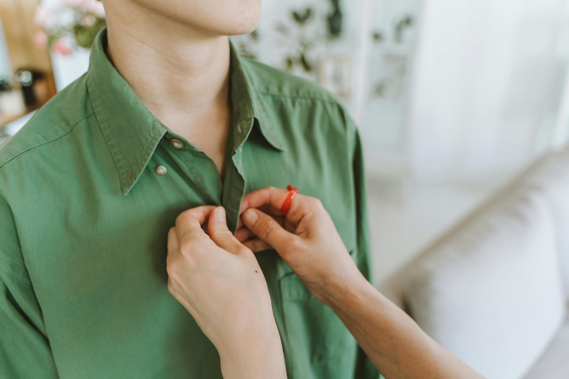 person buttoning green shirt for another person