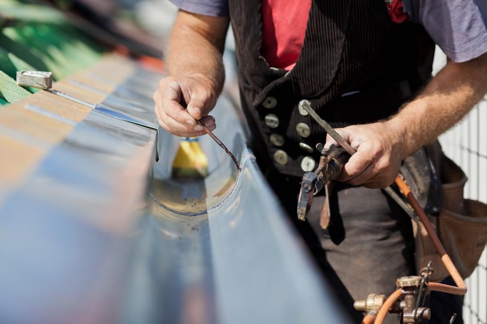 A Man Is Welding a Metal Gutter on A Roof — Top To Bottom Plumbing in Garbutt, QLD