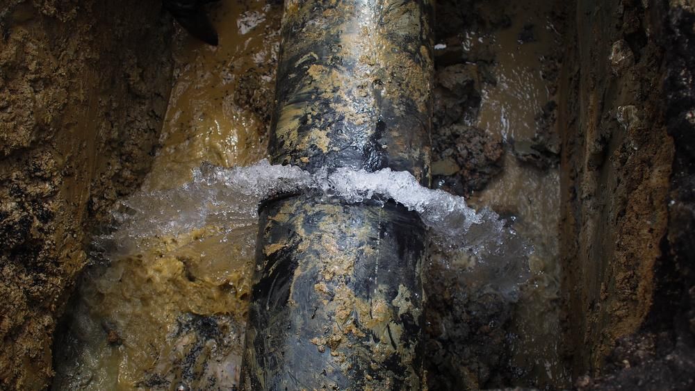 A Pipe Is Leaking Water in A Hole in The Ground — Top To Bottom Plumbing in Garbutt, QLD