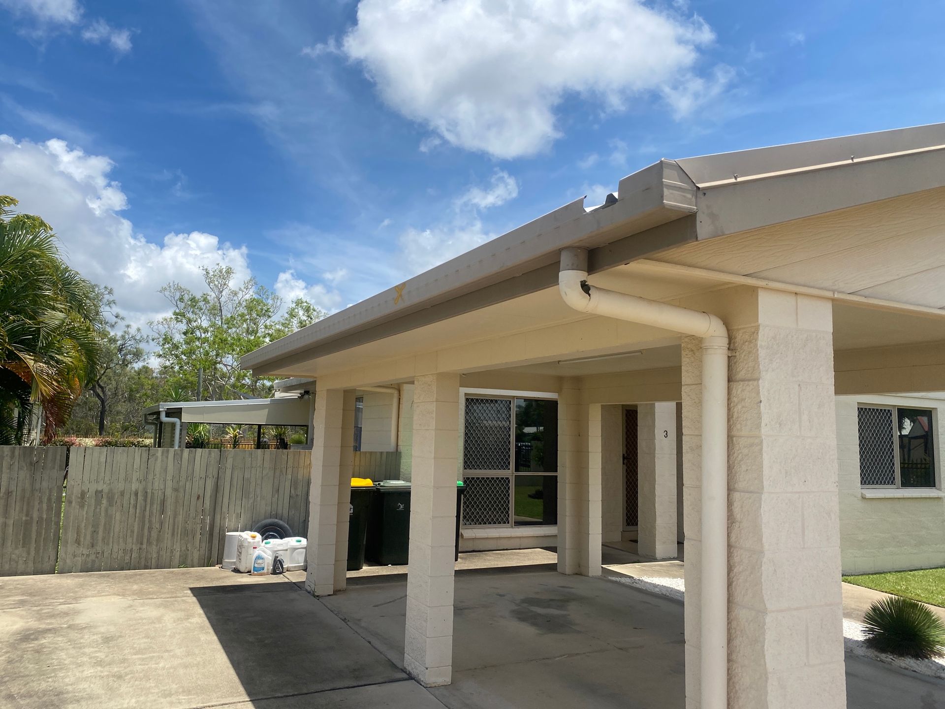 Carport with beige pillars, gutter, and tan roof against a partly cloudy sky — Top To Bottom Plumbing in Garbutt, QLD
