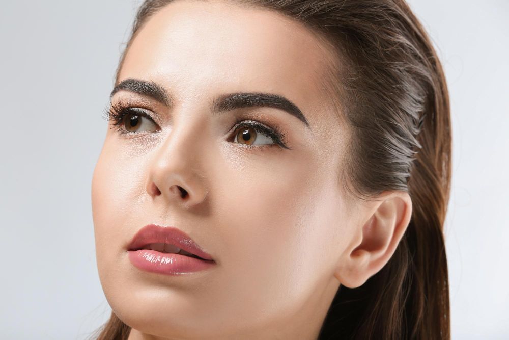 Close-up of a woman with glossy lips and a neutral expression against a light background