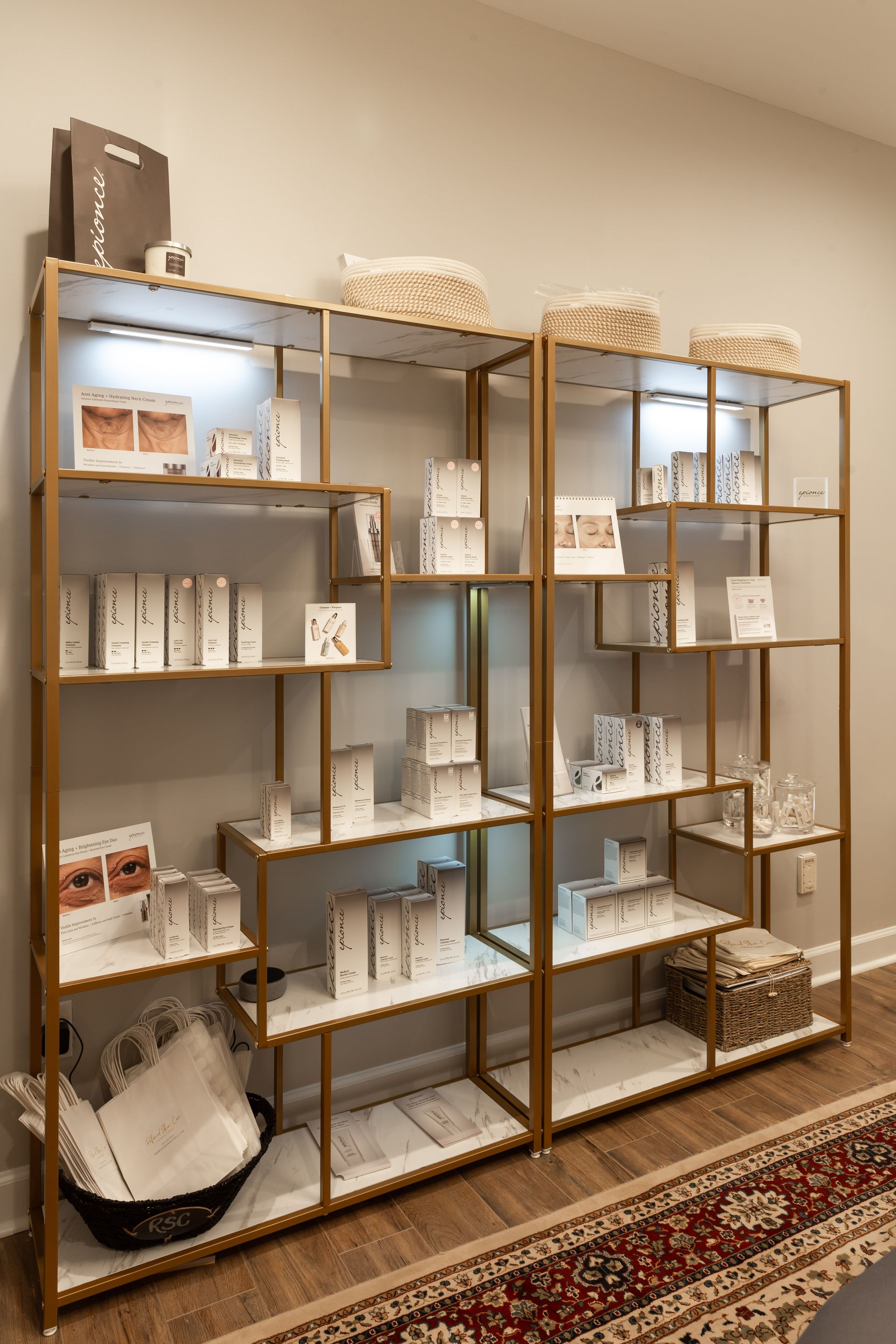 Two gold-framed open shelves displaying various white skincare product bottles and containers against a plain wall.