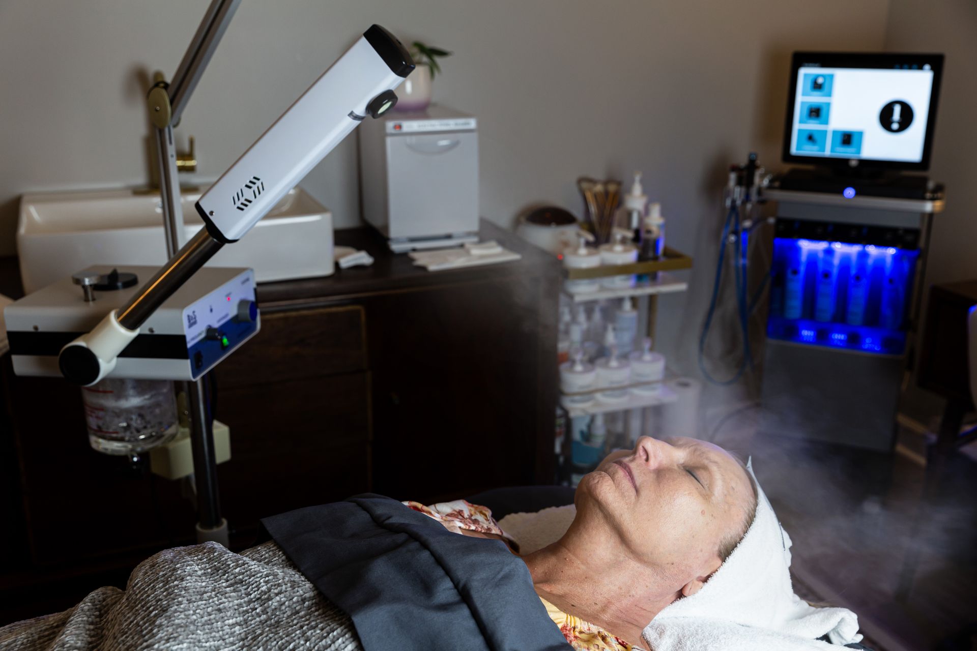 A person lying down receiving a facial treatment with a professional steamer in a spa setting.